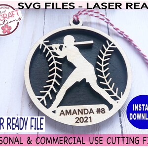 May include: A laser-cut wooden ornament featuring a baseball player silhouette with a baseball stitch design. The ornament is personalized with the name "Amanda #8" and the year "2021".