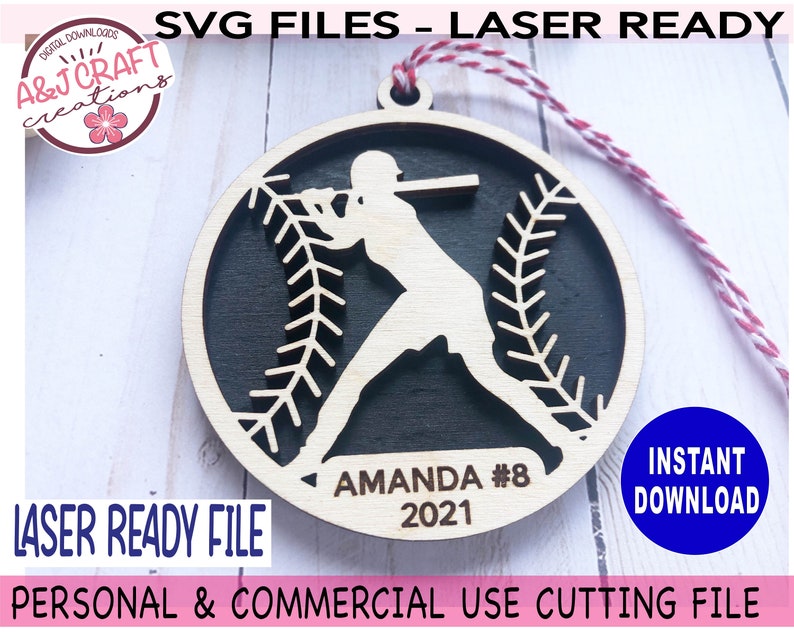May include: A laser-cut wooden ornament featuring a baseball player silhouette with a baseball stitch design. The ornament is personalized with the name "Amanda #8" and the year "2021".