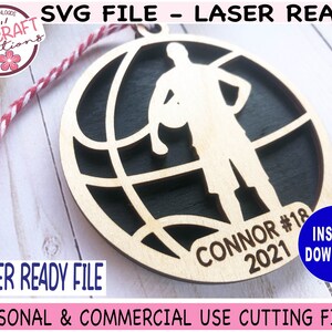 May include: A laser-cut wooden basketball ornament featuring a player silhouette holding a ball within a globe design. The ornament includes the name "CONNOR #18 2021". The design is laser-ready and available for instant download.