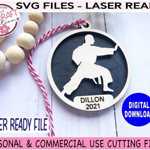 May include: A laser-cut wooden ornament featuring a silhouette of a person in a karate pose. The ornament is black with a white outline and the text "Dillon 2021" is inscribed below the figure.