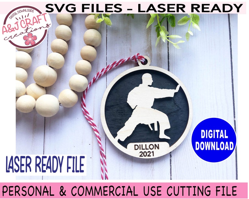 May include: A laser-cut wooden ornament featuring a silhouette of a person in a karate pose. The ornament is black and white and has the name "Dillon" and the year "2021" inscribed on it.