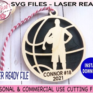 May include: A laser-ready wooden basketball ornament with a player silhouette inside a basketball design. The ornament includes the name "Connor #18 2021". The design is ready for personal and commercial use.