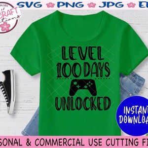 May include: Green t-shirt with black text that reads "Level 100 Days Unlocked" and a black video game controller graphic.  The text is surrounded by a dotted line.