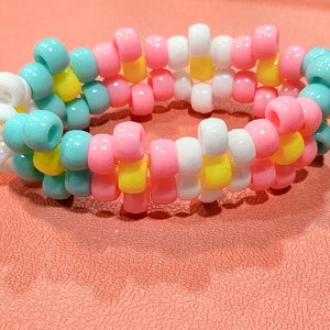 Puede incluir: Un brazalete de cuentas de colores con cuentas turquesa, rosas, blancas y amarillas alternadas.