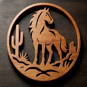 May include: A circular wooden wall art piece featuring a laser-cut design of a horse standing in a desert landscape. The scene includes a saguaro cactus and rocky terrain, all framed within a smooth, polished wood border with a natural grain.