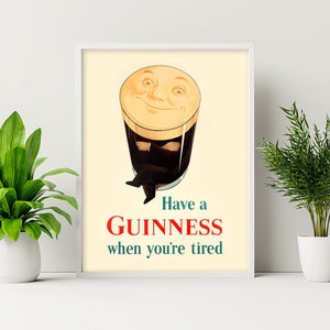 May include: Framed vintage-style Guinness advertisement. The image features a smiling pint of Guinness with arms and legs, above the text "Have a Guinness when you're tired" in red and teal.