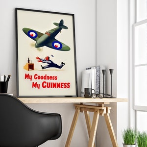 May include: A framed vintage advertisement poster featuring a green airplane with blue and red accents. The poster depicts a man reaching for a falling bottle, with the text "My Goodness My Guinness" in red.