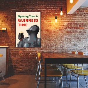 May include: A framed poster with the text "Opening Time is Guinness Time" features a knight in armor holding a pint of dark beer. The poster hangs on a brick wall in a pub setting, with a bar and tables visible.