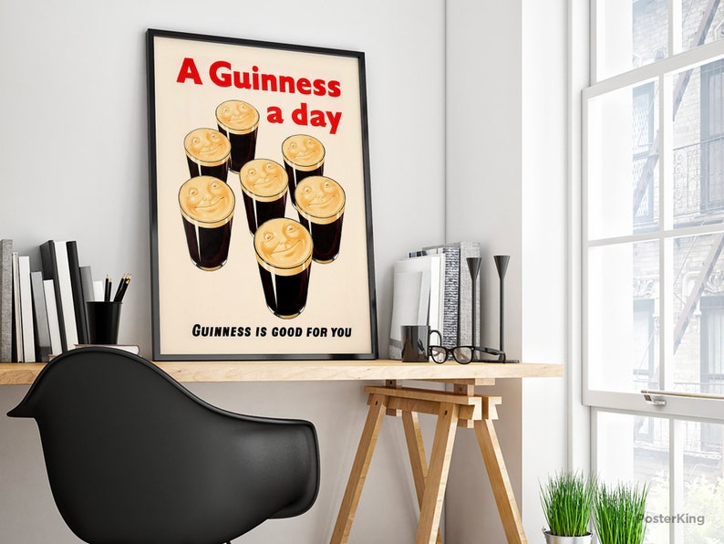 May include: A framed vintage poster featuring the text "A Guinness a day" in red, above cartoon pints of Guinness with smiling faces. The text "Guinness is good for you" is below. The poster is on a wooden desk, with books and a black chair.