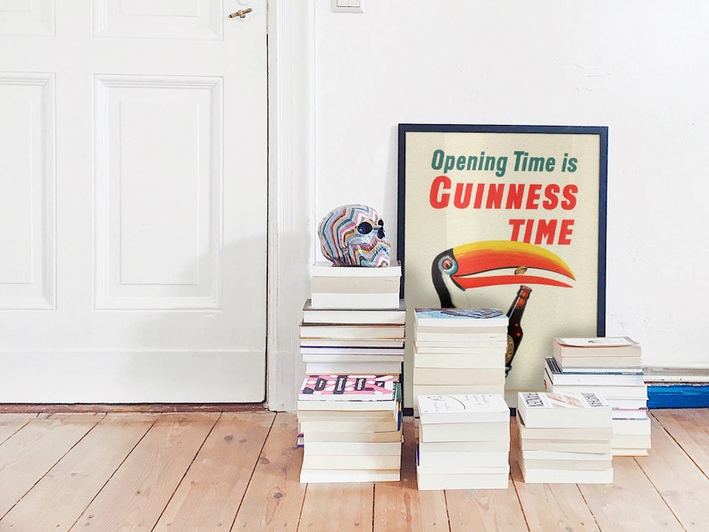 May include: A framed poster with the text "Opening Time is Guinness Time" featuring a toucan with a Guinness bottle. A colourful skull and several stacks of books are in front of a white door and wooden floor.