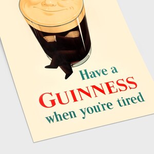 May include: Vintage Guinness advertisement poster. The image features a pint of Guinness with a smiling face and the text "Have a Guinness when you're tired" in red and teal. The poster has a cream-colored background.