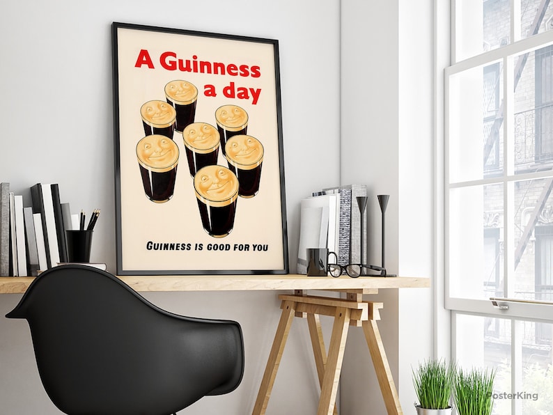 May include: A framed vintage Guinness poster with the text "A Guinness a day" in red, and smiling pints of Guinness. The text "Guinness is good for you" is below the pints. The poster is displayed on a wooden desk, a classic pub-style advertisement.