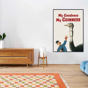May include: A framed vintage advertisement for Guinness stout. The poster features a cartoon illustration of a man in a blue uniform reaching up towards a large bird with the text "My Goodness My Guinness" in red. The background is a cream color.