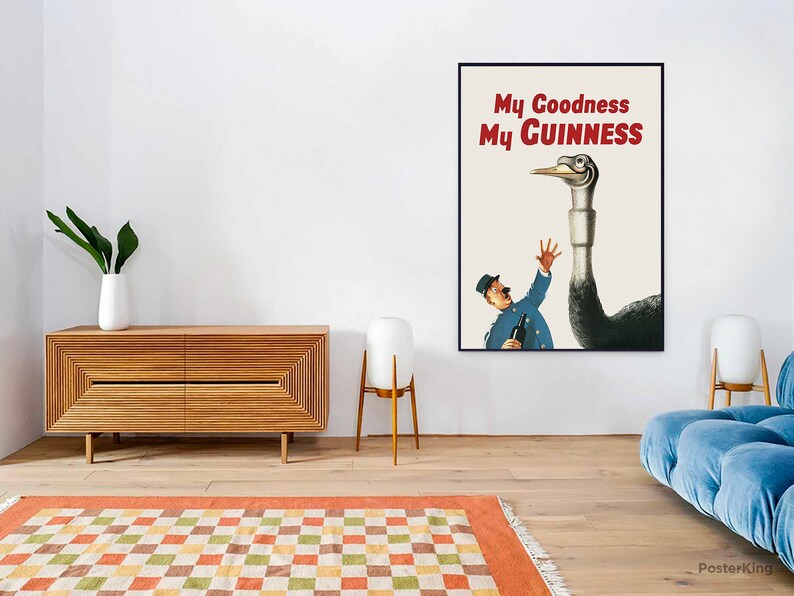 May include: A framed vintage advertisement for Guinness stout. The poster features a cartoon illustration of a man in a blue uniform reaching up towards a large bird with the text "My Goodness My Guinness" in red. The background is a cream color.