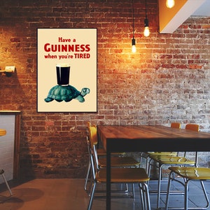Pode incluir: Um p&ocirc;ster de estilo vintage que anuncia a cerveja Guinness. O p&ocirc;ster apresenta uma tartaruga de desenho animado carregando um copo de Guinness com o texto "Have a GUINNESS when you're TIRED".