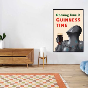 May include: A framed poster with the text "Opening Time is GUINNESS TIME" in red and green. The image features a knight in armor holding a pint of dark beer. The poster is displayed on a white wall in a room with modern furniture.