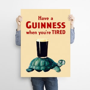 Pode incluir: Um p&ocirc;ster de estilo vintage que anuncia a cerveja Guinness com o texto "Have a GUINNESS when you're TIRED". O p&ocirc;ster apresenta uma ilustra&ccedil;&atilde;o de desenho animado de uma tartaruga carregando um copo de Guinness.