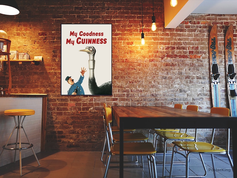 May include: A framed vintage advertisement poster with the text "My Goodness My Guinness" in red. The poster features a cartoon illustration of a man in a blue uniform reaching up towards a large bird-like creature. The background is a brick wall.
