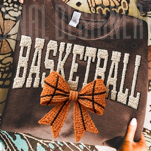 A cozy handmade-style basketball word design with yarn texture and a bow shaped like a basketball. The soft knit details and warm tones create a cozy sporty aesthetic, perfect for basketball-themed crafts and sublimation projects.