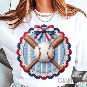 May include: White t-shirt featuring a baseball design. The design includes a baseball, crossed bats, and a bow in red, white, and blue. The baseball is centered on a blue and white striped background, surrounded by a scalloped border.