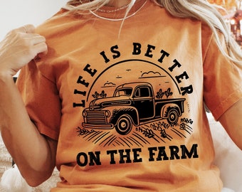 May include: A woman wearing a burnt orange t-shirt with a black graphic of a vintage truck and the text "Life is better on the farm".