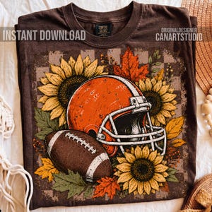 May include: A brown t-shirt featuring a graphic print of an orange football helmet, a brown football, yellow sunflowers, and orange autumn leaves. The text INSTANT DOWNLOAD and ORIGINALDESIGNER CANARTSTUDIO are printed on the shirt.