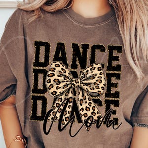 May include: Brown t-shirt with a black and gold graphic that says "Dance Mom" with a leopard print bow in the center.