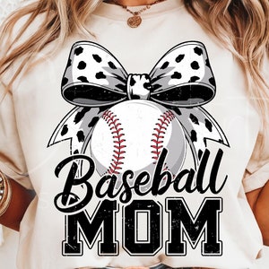 May include: A white t-shirt with a black and white cow print bow and a baseball with red stitching. The text "Baseball Mom" is printed in black with a distressed look.