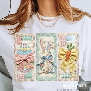 Op de afbeelding: Wit T-shirt met drie applicaties met Pasen-thema: een pastelkleurig ei met een roze strik, een bloemenkonijn met een blauwe strik en een wortel met een gele strik. De tekst "ORIGINAL DESIGNER CANARTS STUDIO" staat onderaan.