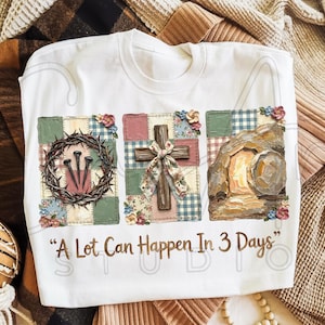 May include: White sweatshirt with a graphic design featuring a crown of thorns, a wooden cross with a bow, and an open tomb. The text "A Lot Can Happen In 3 Days" is printed below the images. The design is set against a patchwork background.