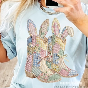 May include: Light blue t-shirt featuring a patchwork design of two cowboy boots with bunny ears. The boots are decorated with floral, gingham, and striped patterns in pastel colors. The text "ORIGINAL DESIGNER CANARTSTUDIO" is visible.