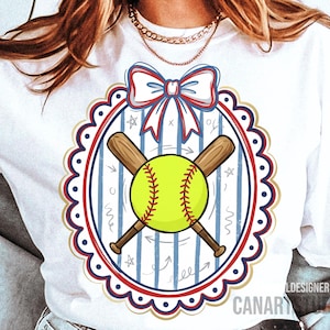 May include: White t-shirt featuring a softball design. The design includes a yellow softball with red stitching, crossed wooden bats, and a decorative oval frame with a red, white, and blue bow. The background has blue stripes and stars.