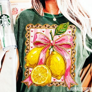 May include: Green t-shirt featuring a lemon design. The design includes a pink bow, yellow lemons, and a pink and white striped background with red hearts. The design is framed with a leopard print border.