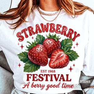May include: White t-shirt with a red strawberry design. The graphic includes the word "STRAWBERRY", three strawberries, green leaves, and the text "EST 1968 FESTIVAL A berry good time."