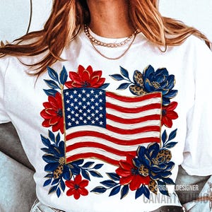 May include: White t-shirt featuring a vibrant American flag design. The flag is surrounded by red and blue floral accents with gold leopard print details. The design includes the text "ORIGINAL DESIGNER CANARY BLANK".