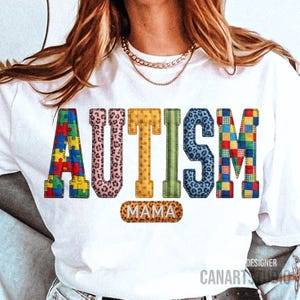 Puede incluir: Camiseta blanca con la palabra "AUTISMO" en letras coloridas estilo patchwork. La letra "A" es un diseño de rompecabezas. Debajo, "MAMA" en un óvalo con estampado de leopardo.