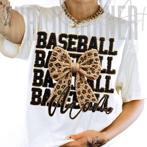 May include: White t-shirt with the words "BASEBALL MOM" in black, outlined in gold. The word "BASEBALL" is stacked three times above the word "MOM". A large bow with a leopard print design is centered on the shirt.