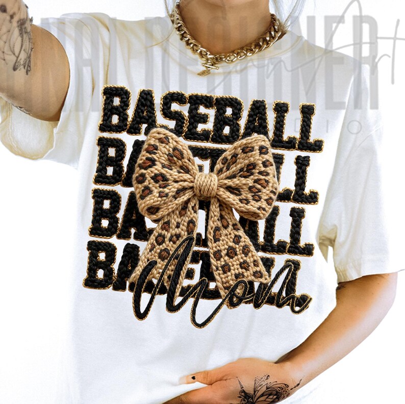 May include: White t-shirt with the words "BASEBALL MOM" in black, outlined in gold. The word "BASEBALL" is stacked three times above the word "MOM". A large bow with a leopard print design is centered on the shirt.