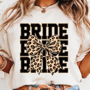 May include: White t-shirt with the word "BRIDE" printed in black with a leopard print bow in the centre.