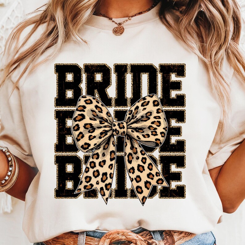 May include: White t-shirt with the word "BRIDE" printed in black with a leopard print bow in the centre.