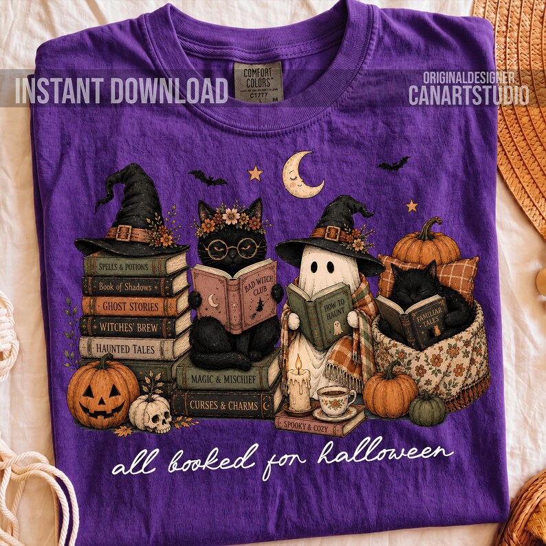 May include: A purple t-shirt featuring a graphic of a black cat and a ghost wearing witch hats, reading books. The design includes stacks of books, pumpkins, a skull, and a crescent moon. The text reads "all booked for halloween".