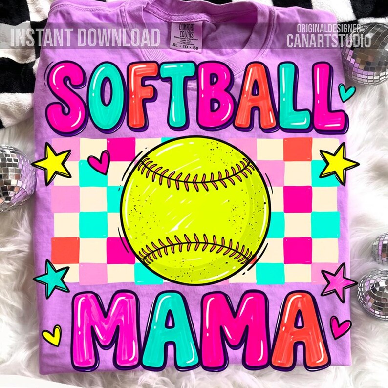 May include: A lilac-colored t-shirt with the words "SOFTBALL MAMA" in a colorful, bubble-letter style. A yellow softball is centered on the shirt, with a checkered pattern in the background. The shirt also features star and heart graphics.