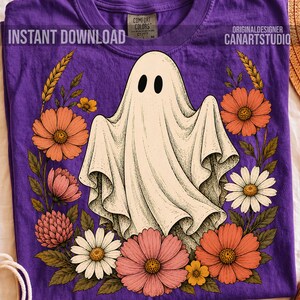 May include: A purple t-shirt featuring a central graphic of a white ghost surrounded by a wreath of colorful flowers including orange, pink, and white daisies. The text INSTANT DOWNLOAD and ORIGINALDESIGNER CANARTSTUDIO appear on the shirt.