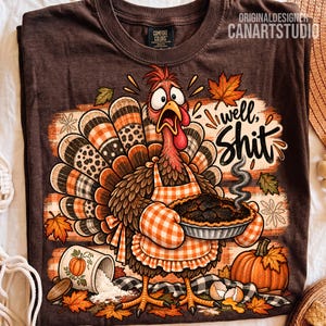 May include: A dark brown t-shirt featuring a cartoon turkey wearing an orange and white checkered apron and oven mitts, holding a steaming burnt pie. The graphic includes the text well, Shit, a spilled flour container, a pumpkin, and autumn leaves.