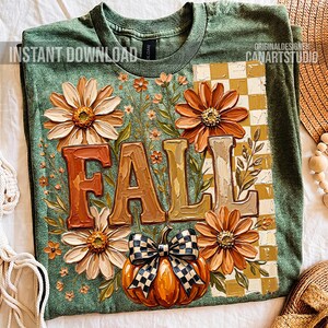 May include: Green t-shirt with a fall-themed design. The design features the word "FALL" in large, textured letters, surrounded by orange and cream-colored flowers, a pumpkin with a checkered bow, and a checkered pattern.