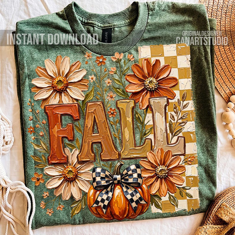 May include: Green t-shirt with a fall-themed design. The design features the word "FALL" in large, textured letters, surrounded by orange and cream-colored flowers, a pumpkin with a checkered bow, and a checkered pattern.