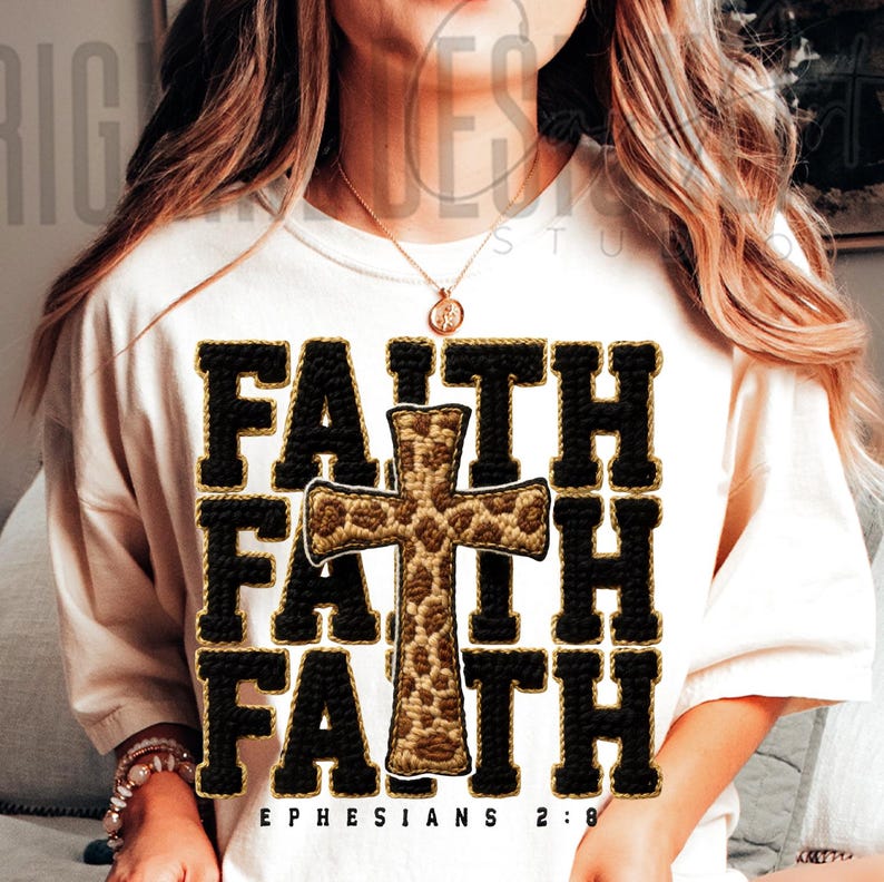 May include: Cream-colored t-shirt with the word "FAITH" in a repeating pattern, with a cross in the center. The cross and the word "FAITH" are in black with a gold trim. The text "EPHESIANS 2:8" is at the bottom.