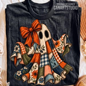 May include: A dark charcoal gray t-shirt featuring a graphic of a ghost made of patchwork fabric squares in orange, blue, and green with floral and gingham patterns. The ghost has a large orange bow and the text ORIGINALDESIGNER CANARTSTUDIO.