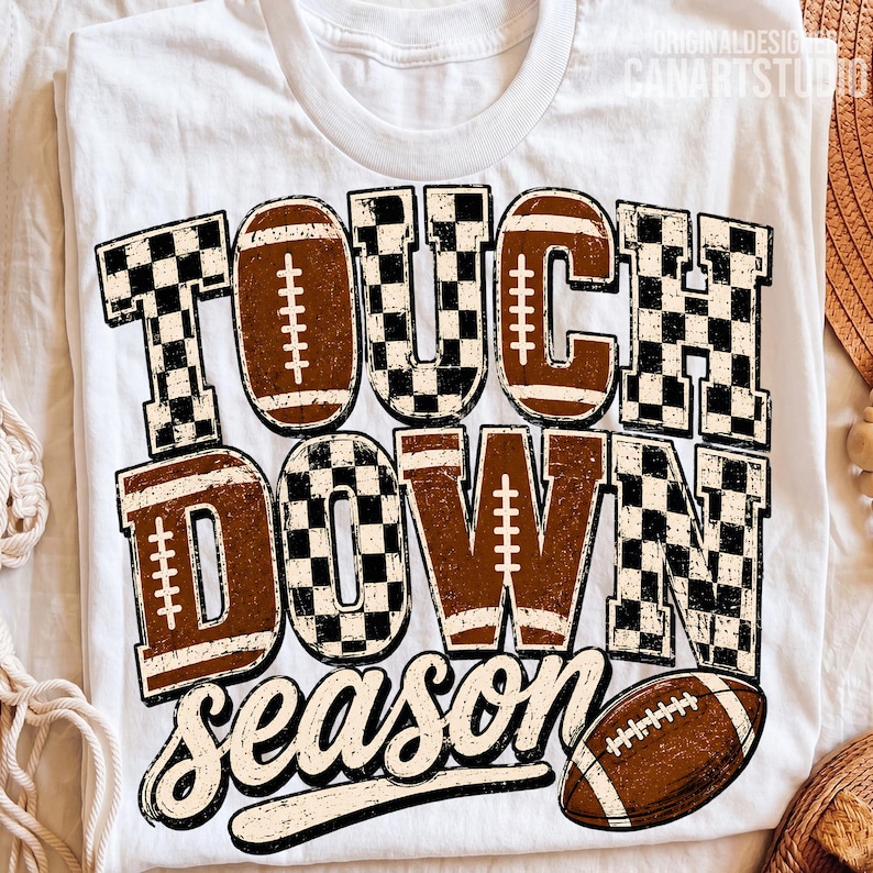 May include: A white t-shirt featuring the text TOUCH DOWN SEASON in a distressed brown and black checkered pattern. The letters incorporate football graphics with white laces. A brown football is positioned below the text.