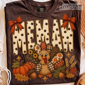 May include: A dark brown t-shirt featuring the text MEMAW in cream with brown polka dots, accented by two orange bows. Below, a turkey illustration with patterned feathers sits beside a pumpkin, acorns, wheat stalks, and autumn leaves.